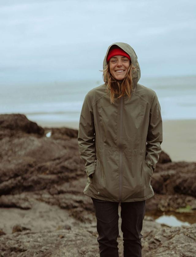 A girl at the seaside wearing a raincoat and smiling into the camera.