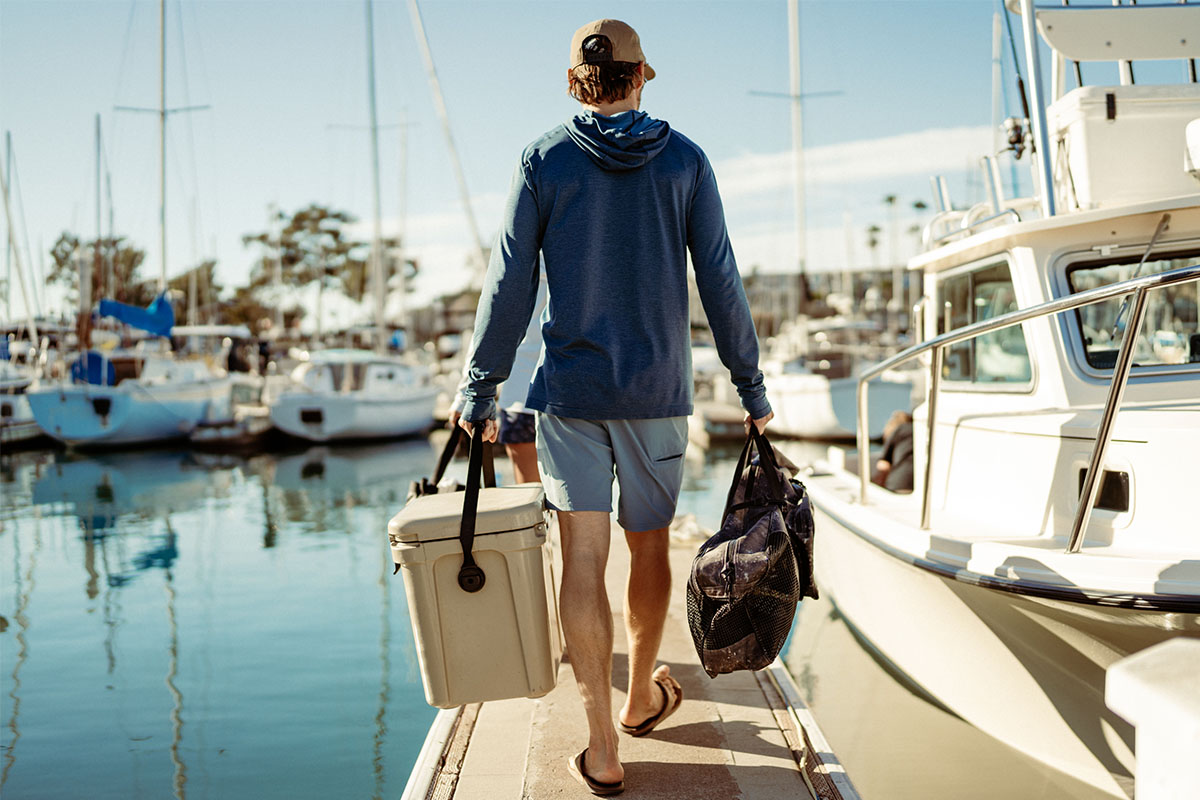 A man carries a dry well and a bag down the pier, wearing KUHL UPF Clothing to prevent skin cancer and melanoma