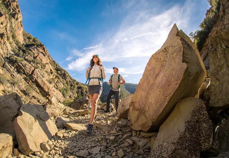 KUHL summer hiking clothing for men and women show by a man and a woman hiking on a rocky trail