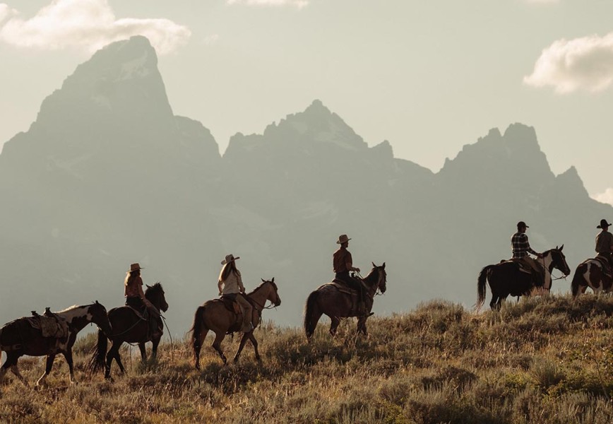 Reining in a Passions - Silhouettes of horses and riders on a hill with mountains in the backdrop